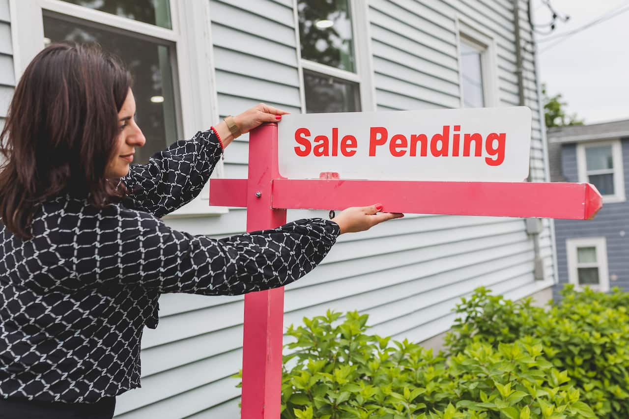 A realtor adjusting a sale pending sign outside a house for sale