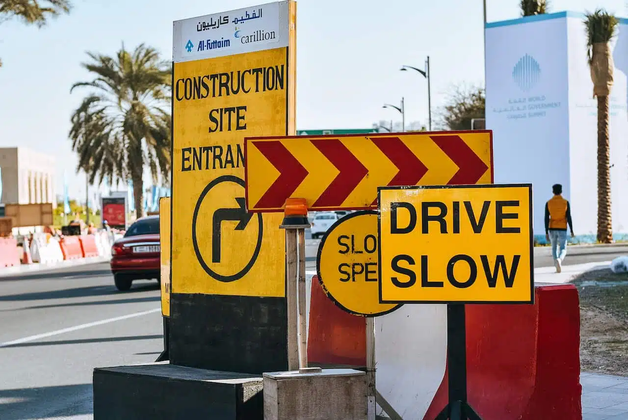 Yellow construction and caution signs on a city street warn of roadwork. Drive slow for safety
